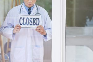 Doctor holding sign that reads "Closed"